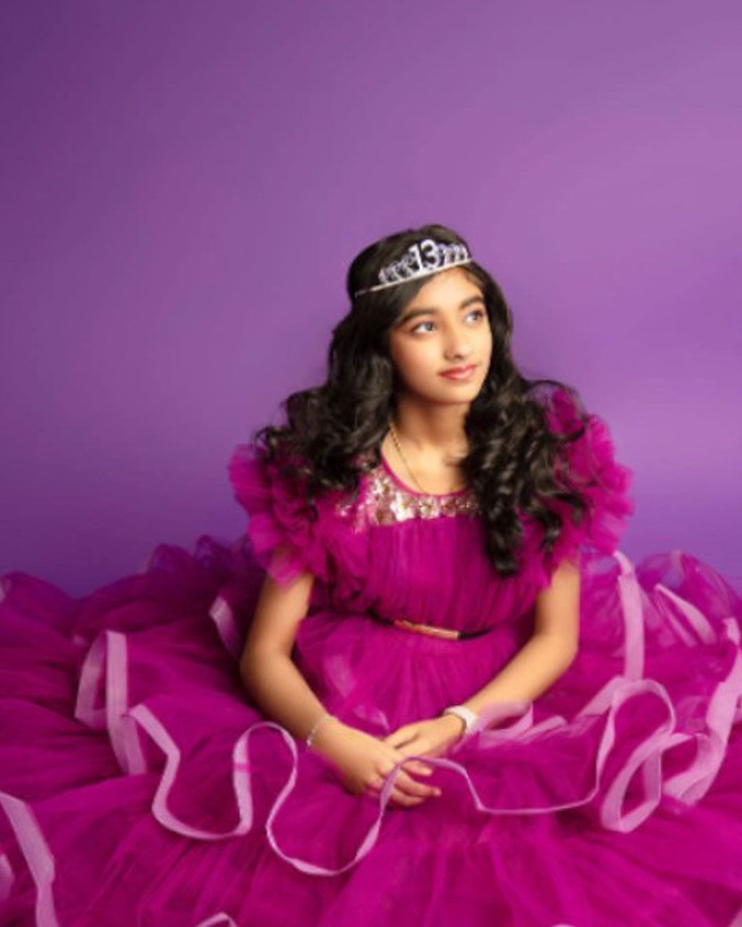 A girl in a purple dress and tiara is sitting on the floor