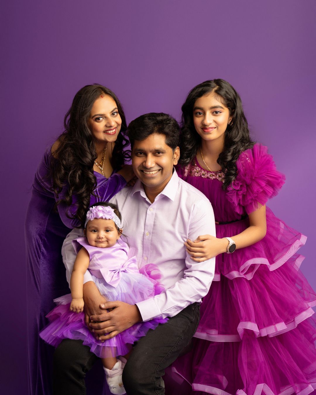 A family is posing for a picture in front of a purple background