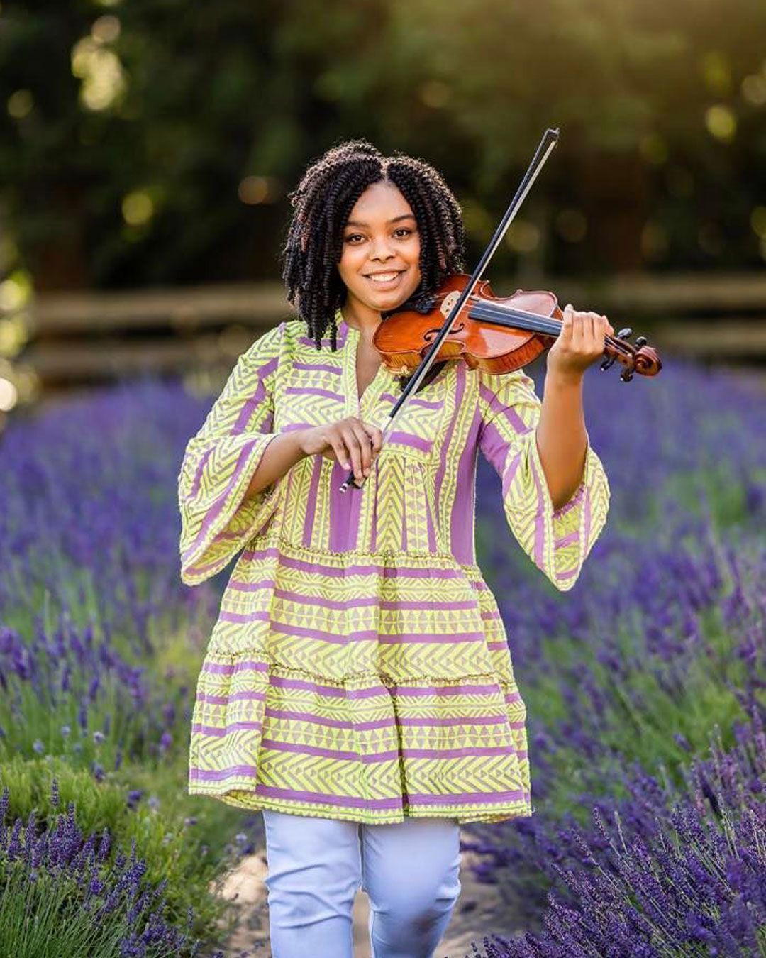 A young woman is standing in a field of lavender holding a violin.