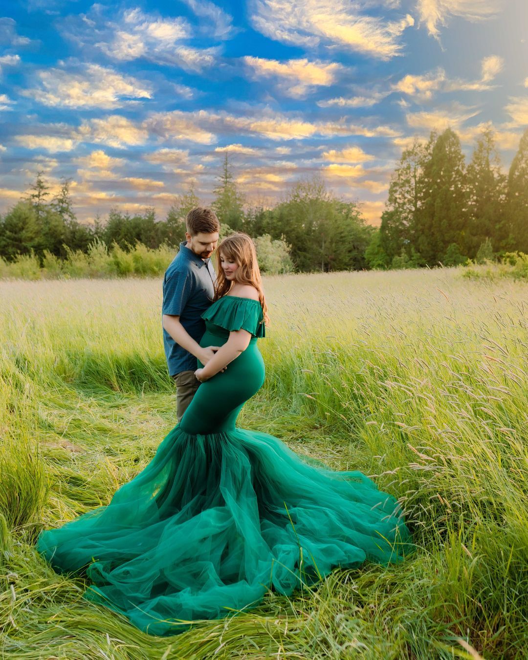 A pregnant woman in a green dress is standing next to a man in a field