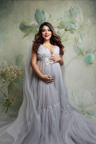 A pregnant woman is wearing a long gray dress and holding her belly