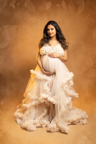 A pregnant woman is wearing a white dress and holding her belly