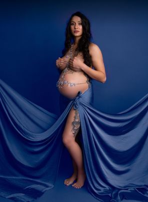 A pregnant woman is standing in front of a blue cloth