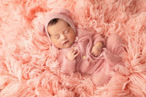 A newborn baby is sleeping on a pink blanket