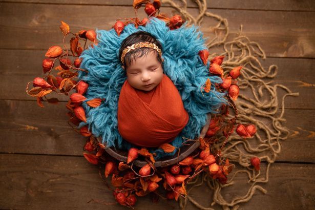A newborn baby wrapped in an orange and blue blanket is sleeping in a basket