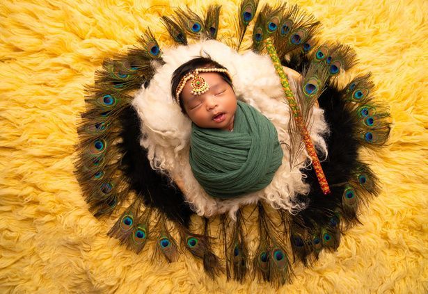 A newborn baby is wrapped in a green blanket and surrounded by peacock feathers