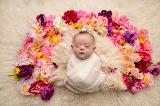 A baby wrapped in a white blanket is laying on a pile of flowers
