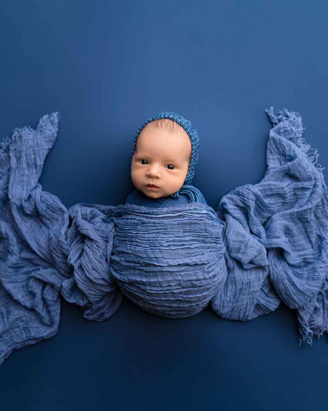 A newborn baby wrapped in a blue blanket on a blue background