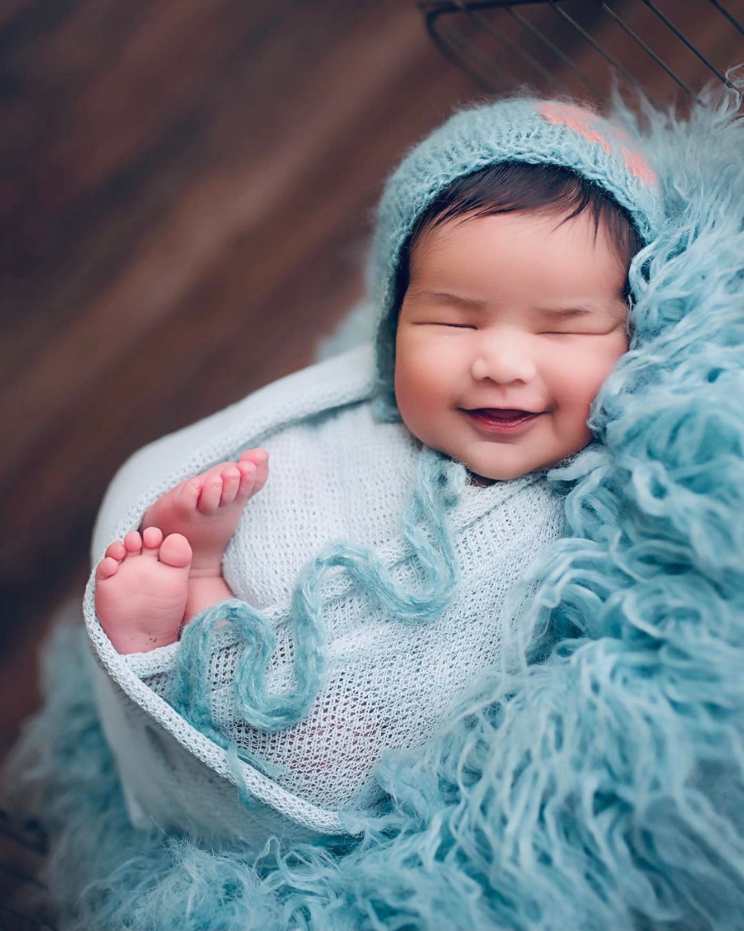 A newborn baby is wrapped in a blue blanket and smiling