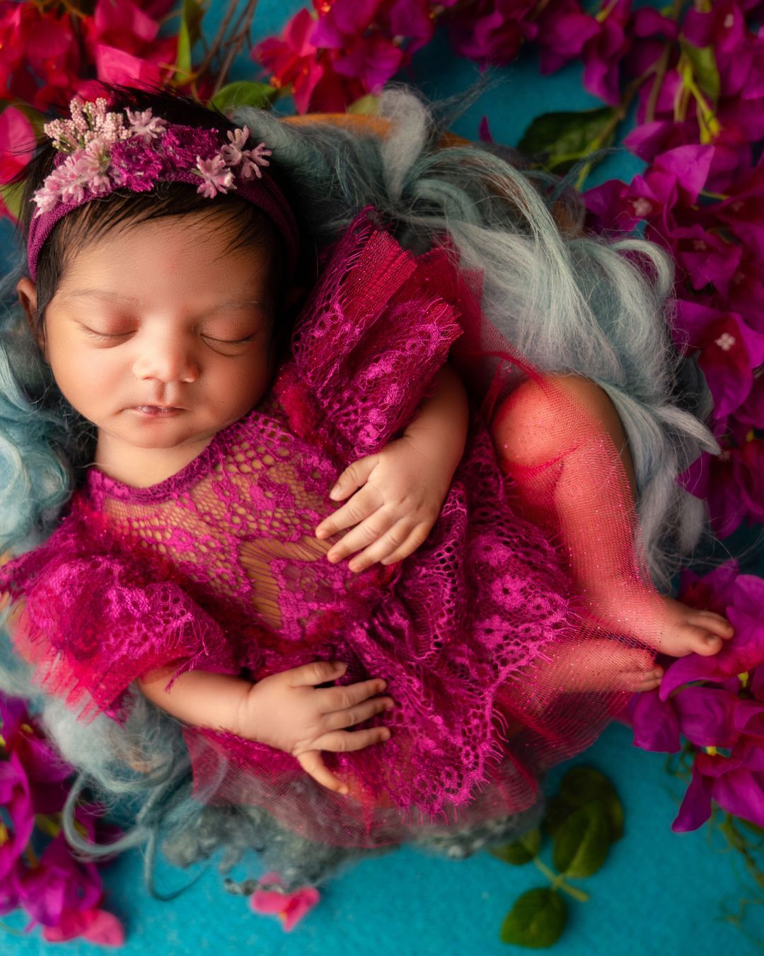 A newborn baby girl is sleeping in a pink dress surrounded by flowers