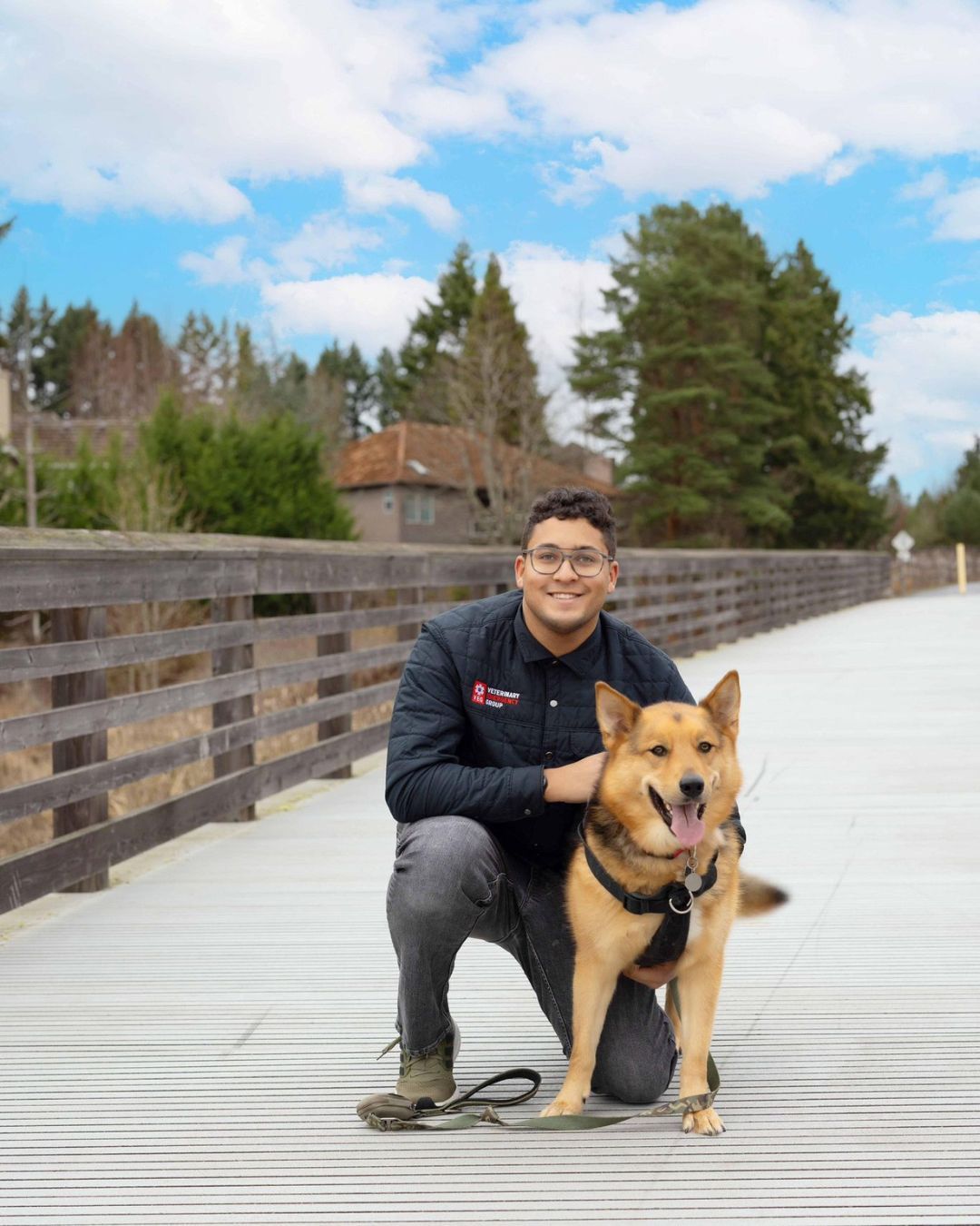 A man is kneeling down next to a dog on a wooden bridge