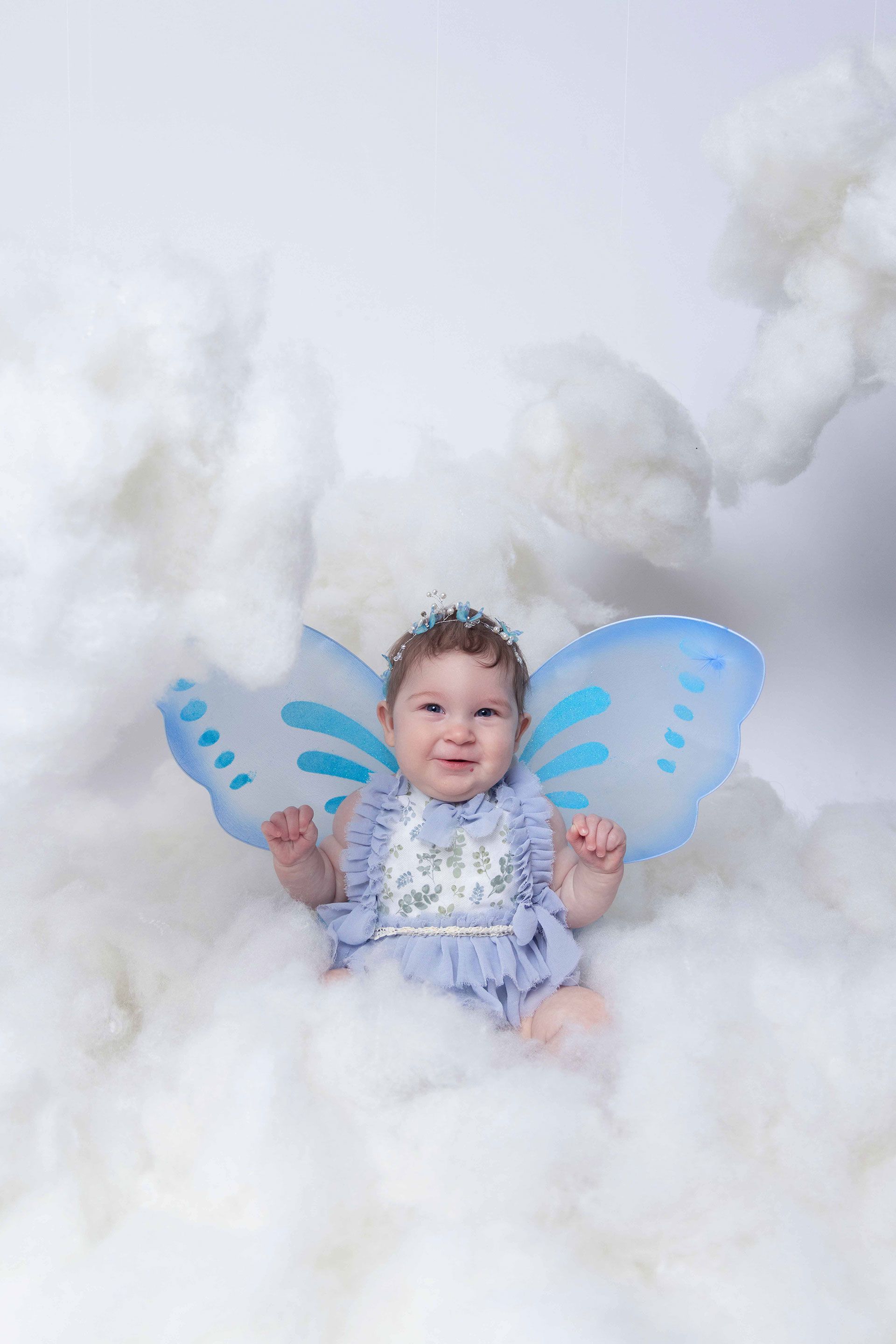 A baby girl wearing fairy wings is sitting in the clouds
