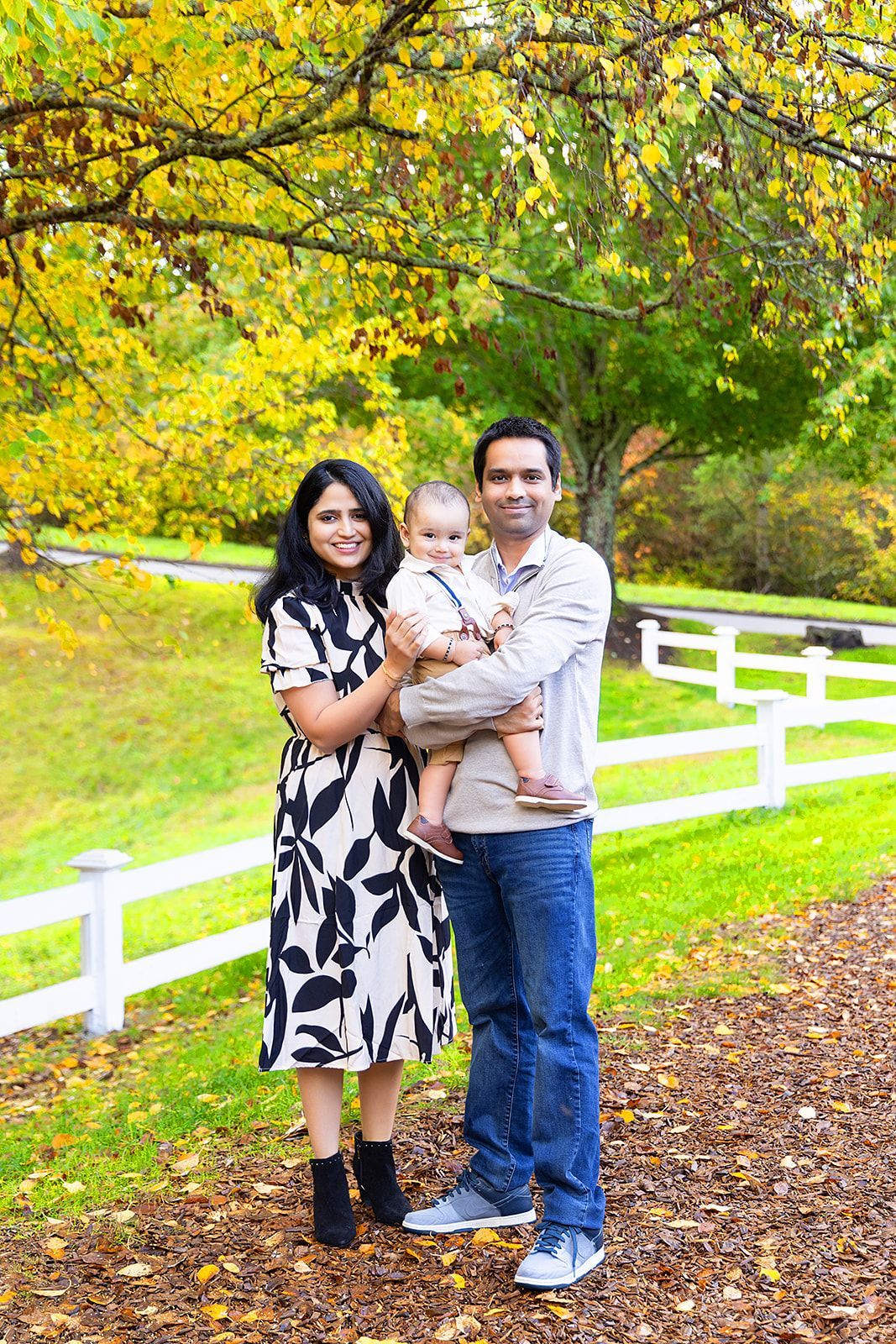 A family is posing for a picture in front of a white fence in a park.