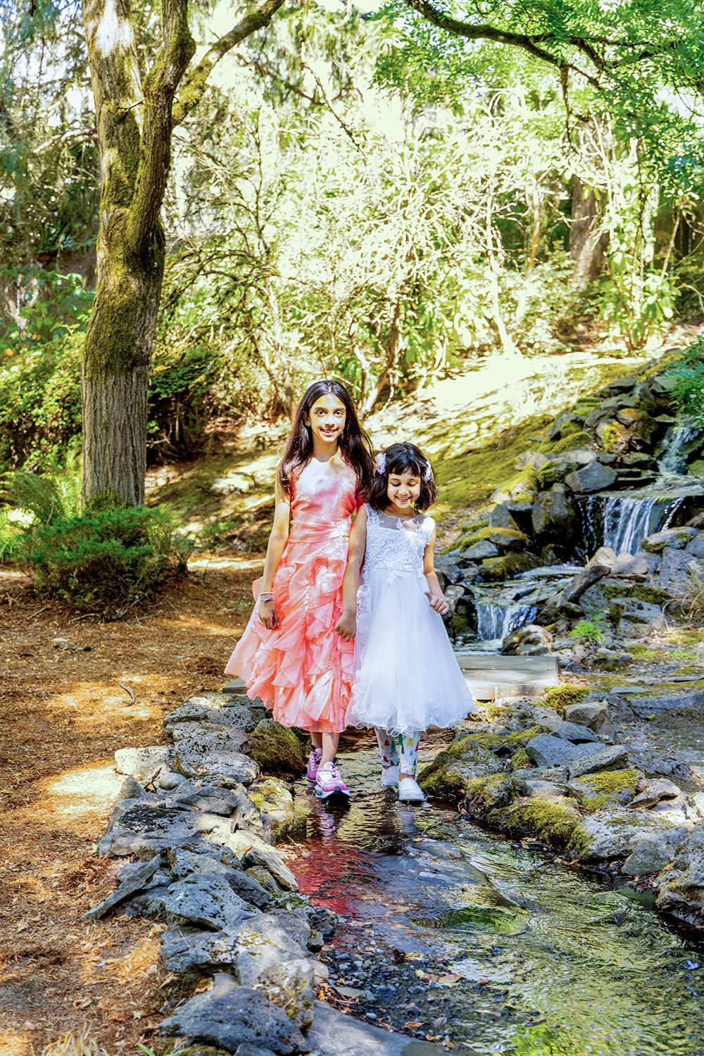Two little girls in dresses are standing next to a stream