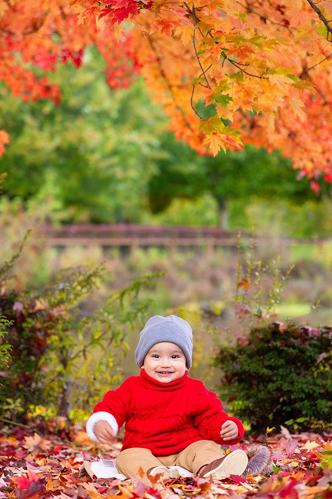 A baby is sitting in a pile of leaves under a tree