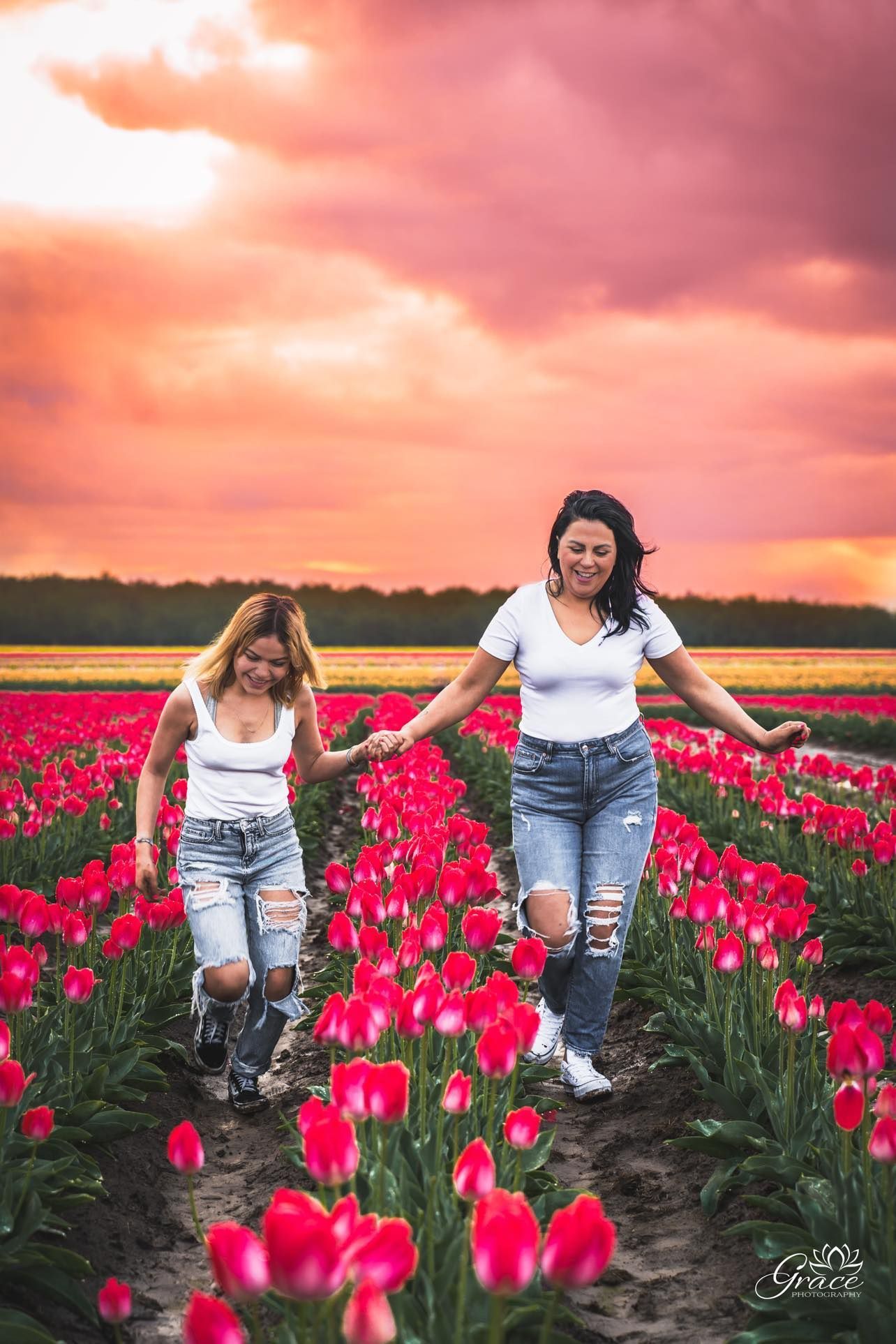 Two women are walking through a field of red tulips holding hands