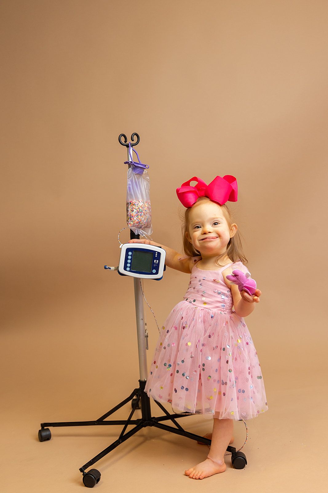 A little girl in a pink dress is standing next to a medical device