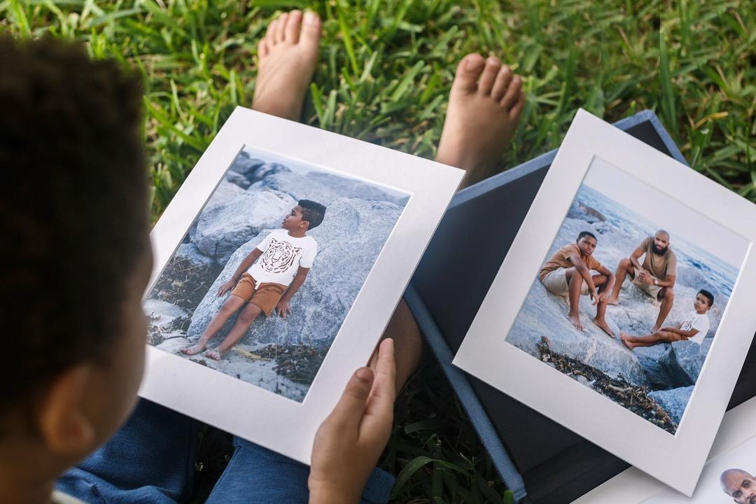 A young boy is sitting on the grass holding two framed pictures