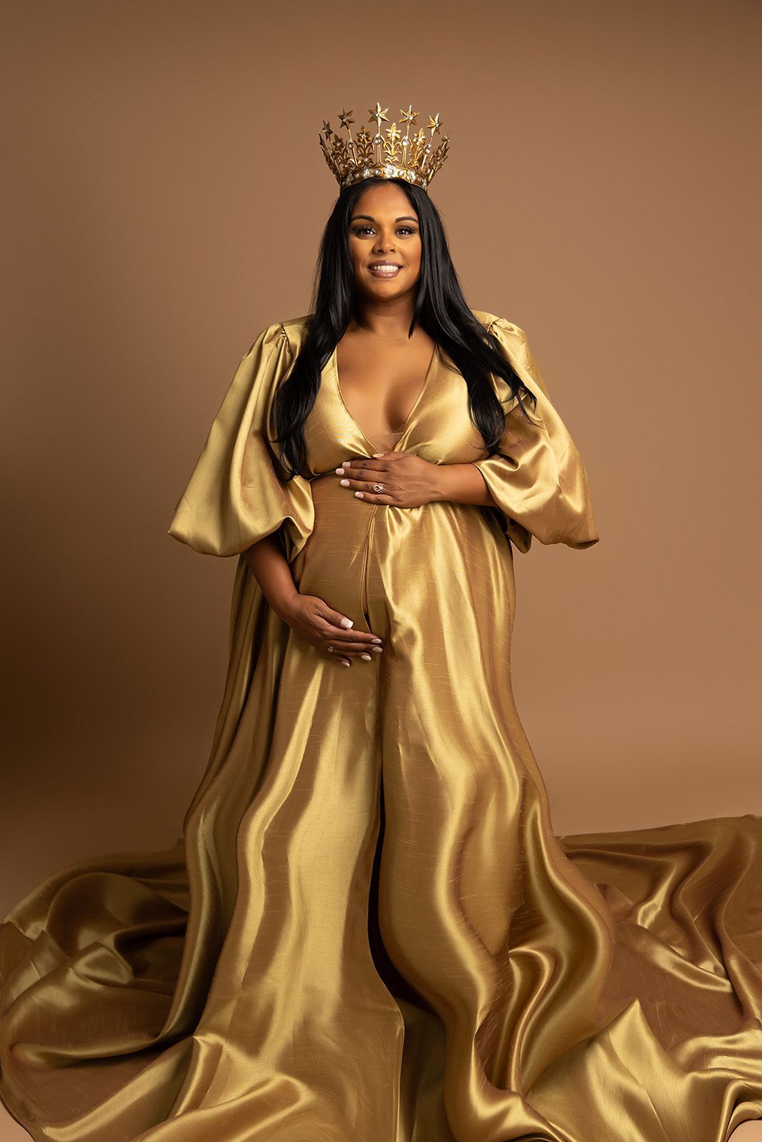 A pregnant woman is wearing a gold dress and a crown