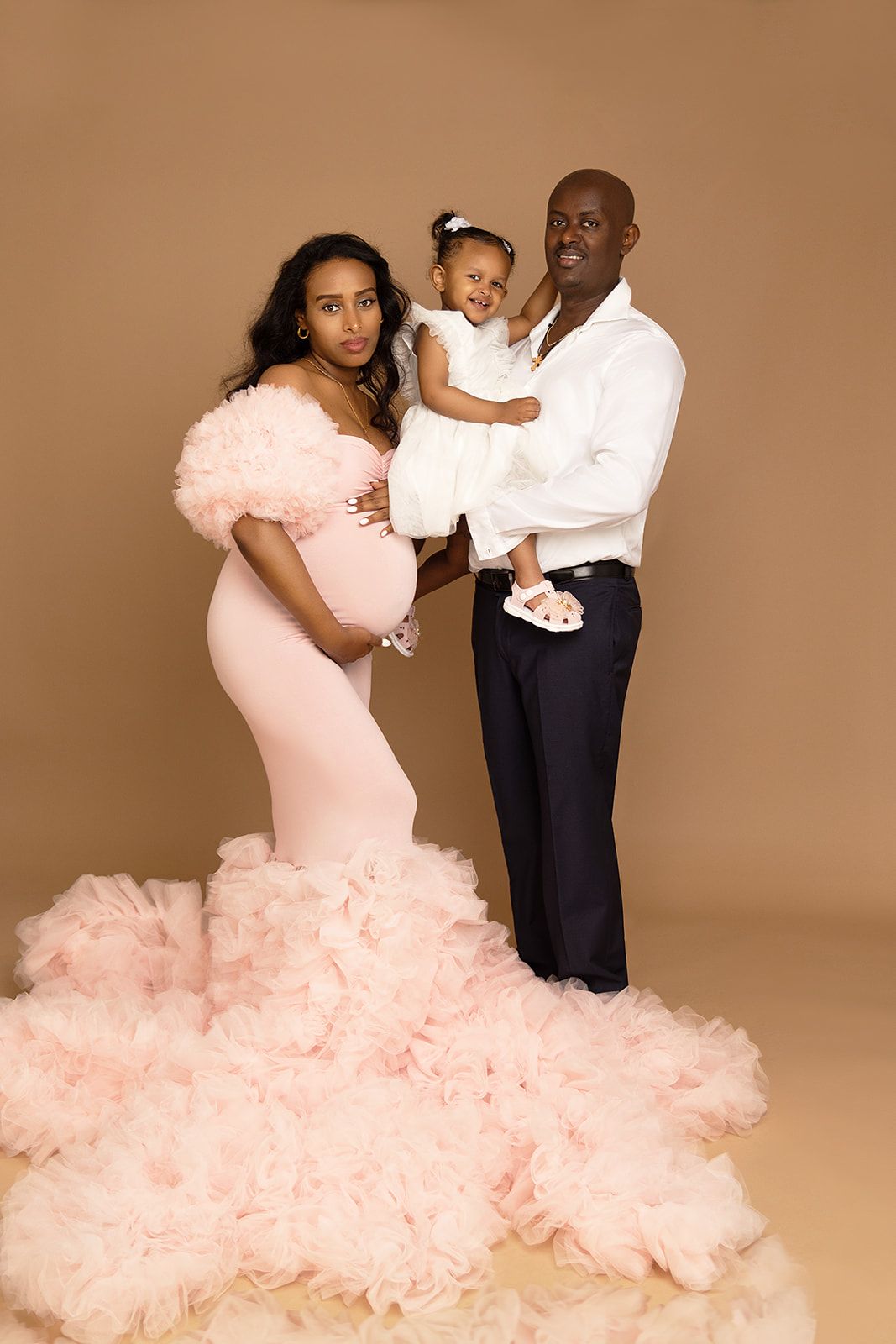 A pregnant woman is posing for a picture with her husband and daughter