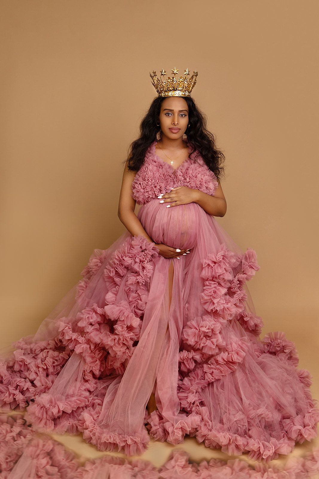 A pregnant woman is wearing a pink dress and a crown