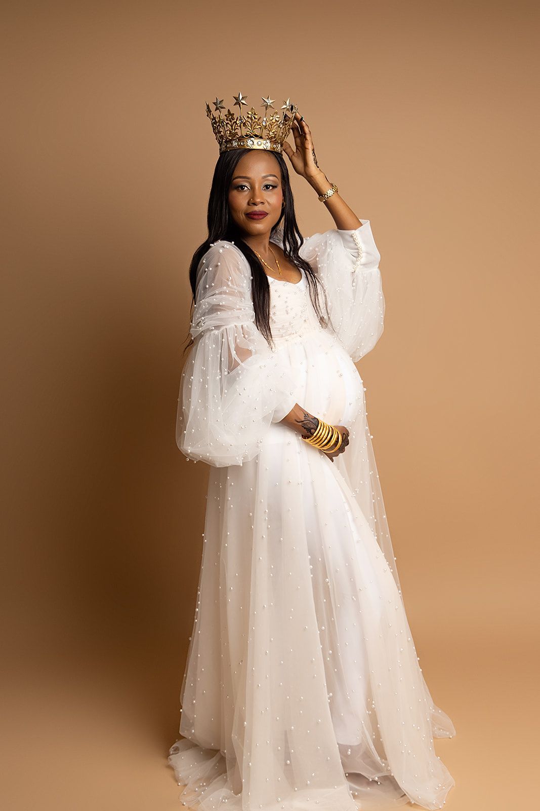 A pregnant woman in a white dress is wearing a crown