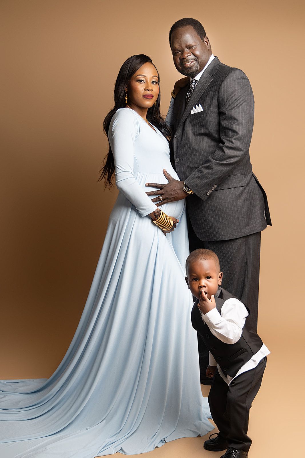 A pregnant woman is posing for a picture with her husband and son