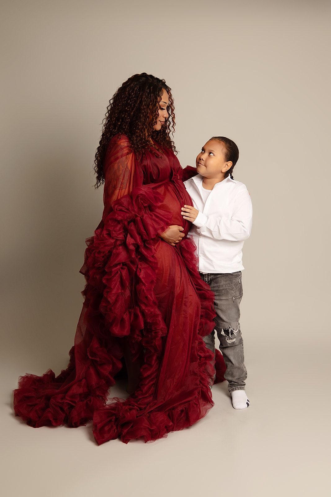 A pregnant woman in a red gown is standing next to a little boy