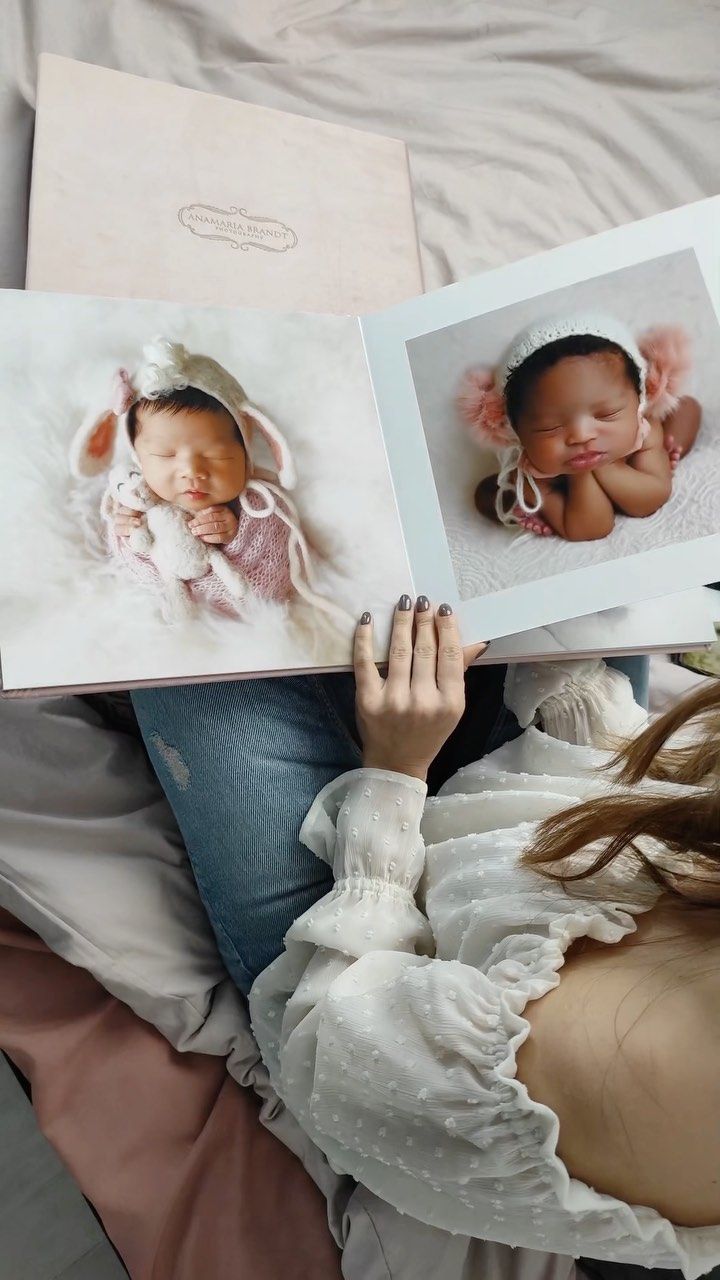A woman is laying on a bed holding a book with two pictures of a baby
