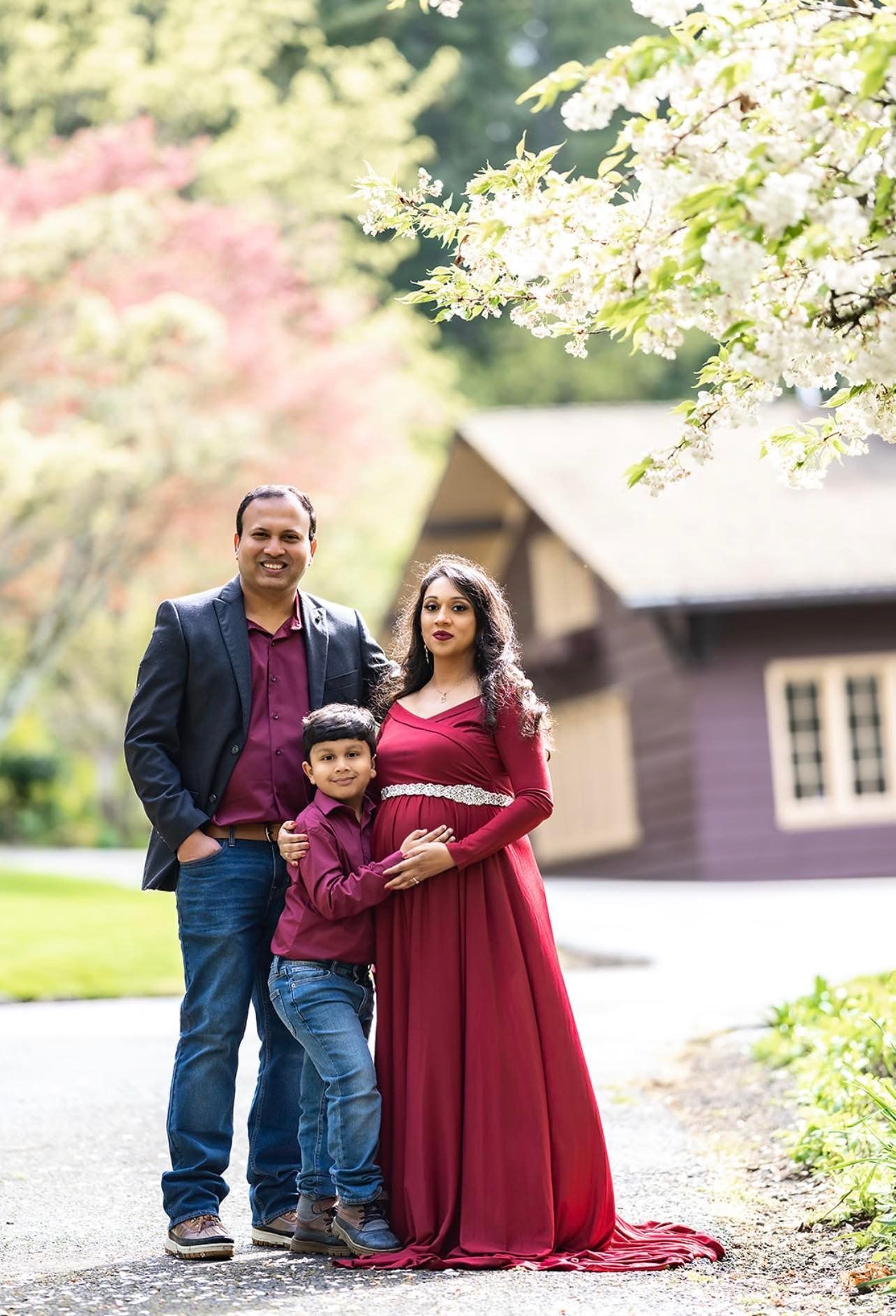 A pregnant woman in a red dress is posing for a picture with her husband and son