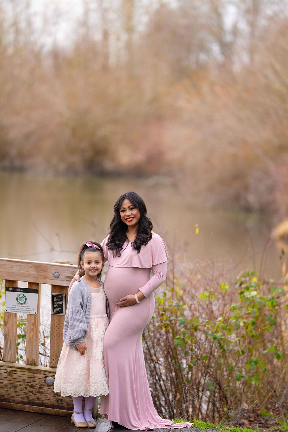 A pregnant woman is standing next to a little girl on a bridge