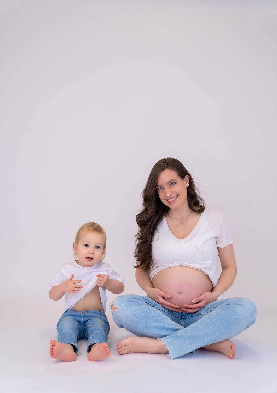 A pregnant woman is sitting on the floor next to a baby