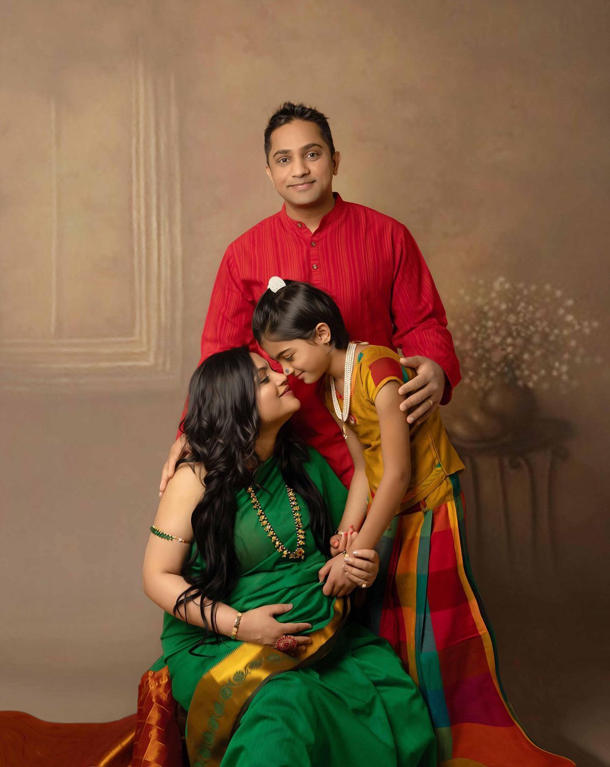 A pregnant woman in a green saree is posing for a picture with her husband and daughter