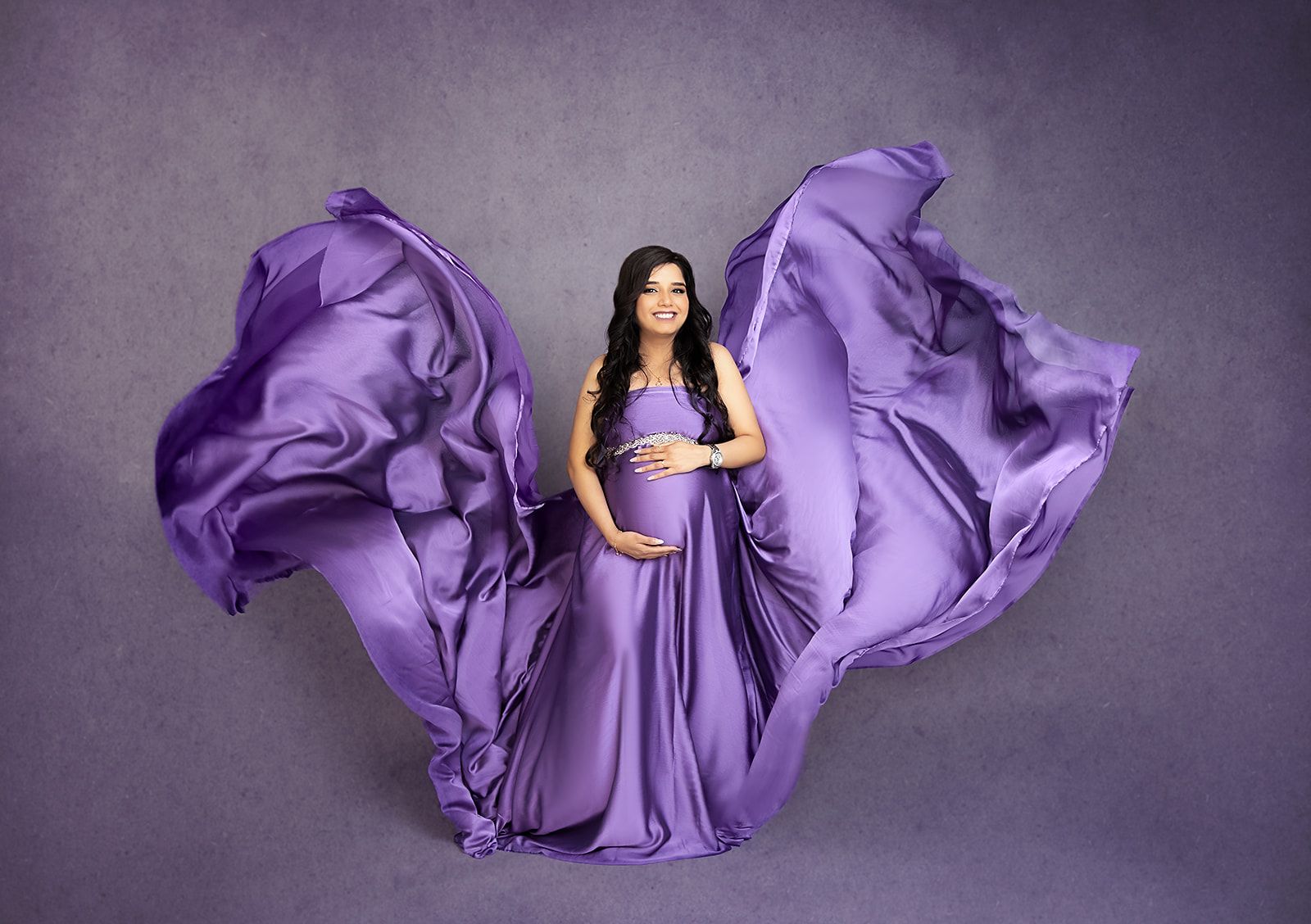 A pregnant woman in a purple dress is holding her belly