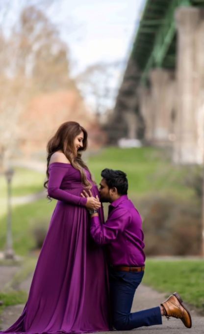 A man is kneeling down next to a pregnant woman in a purple dress