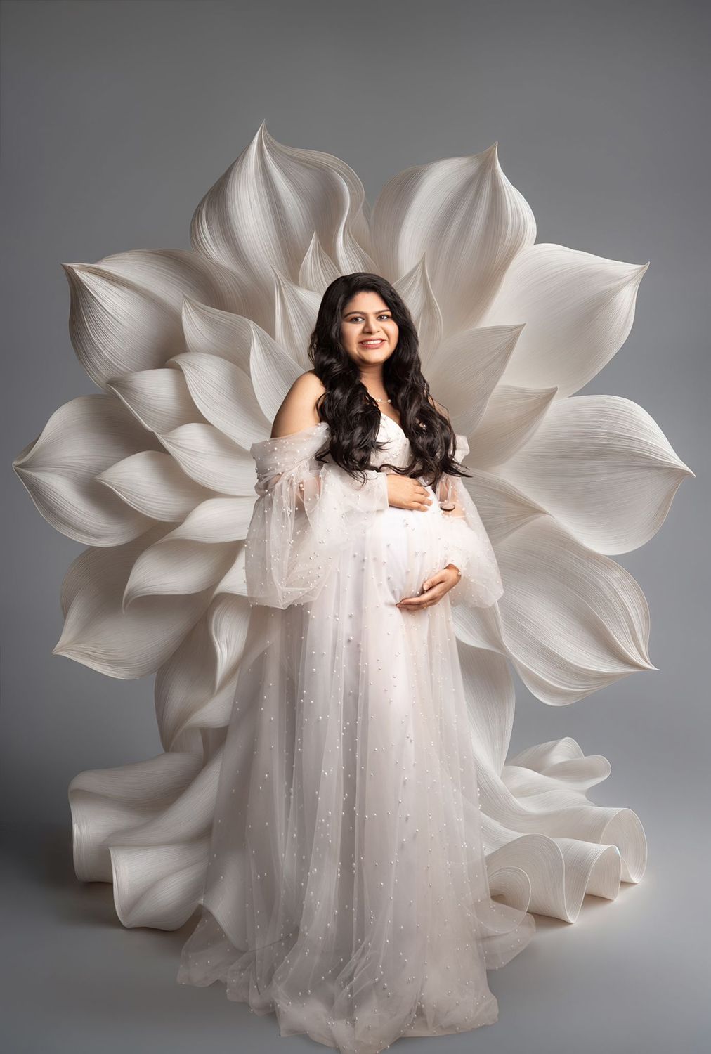 A pregnant woman in a white dress is standing in front of a large white flower