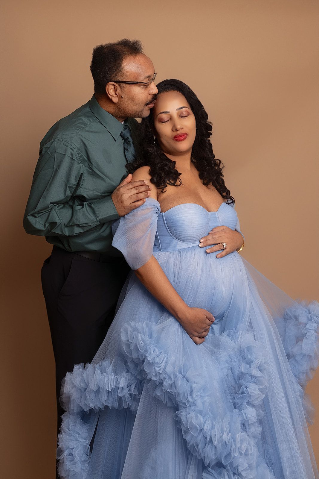 A man is kissing a pregnant woman on the cheek.