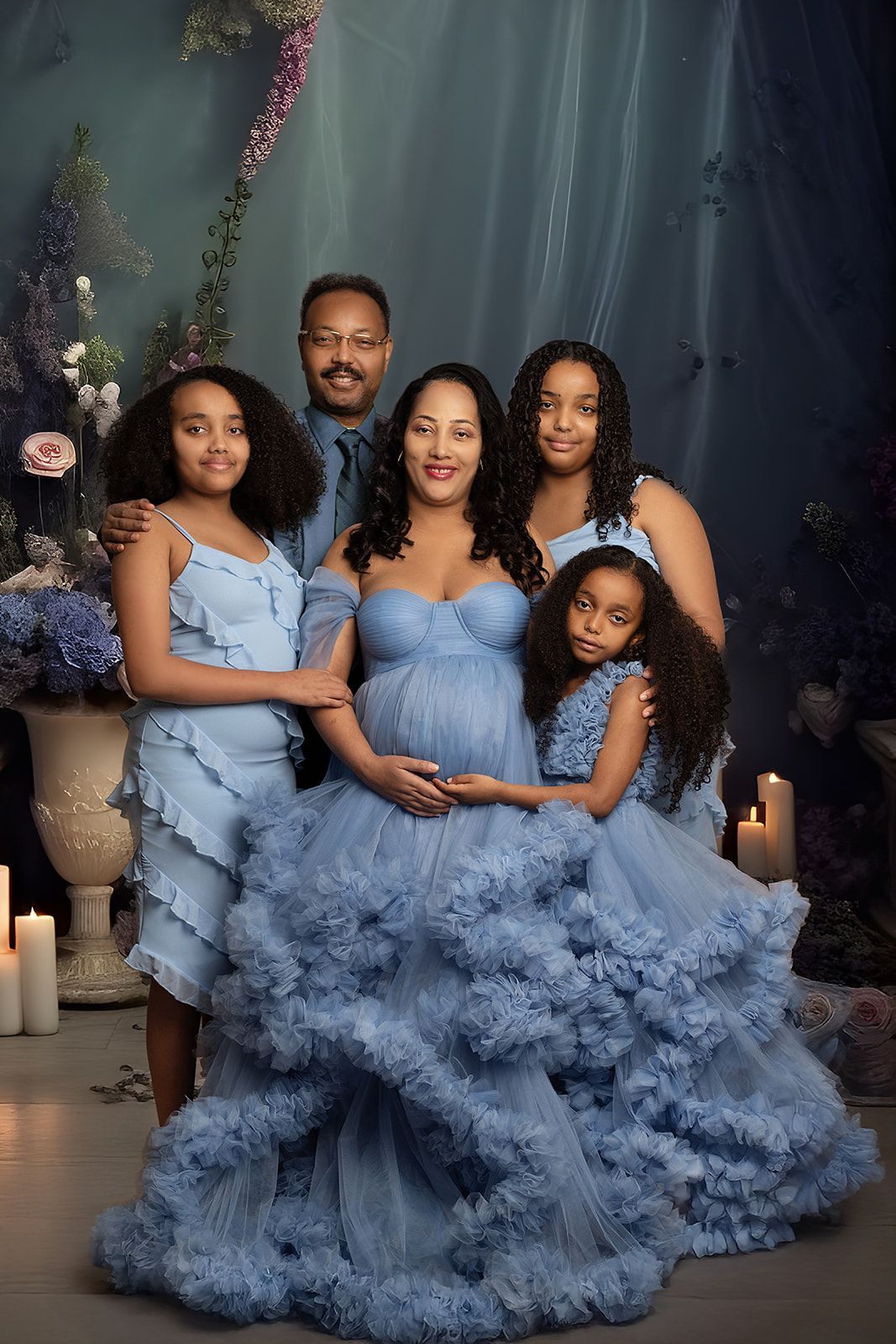 A pregnant woman in a blue dress is posing for a picture with her family.