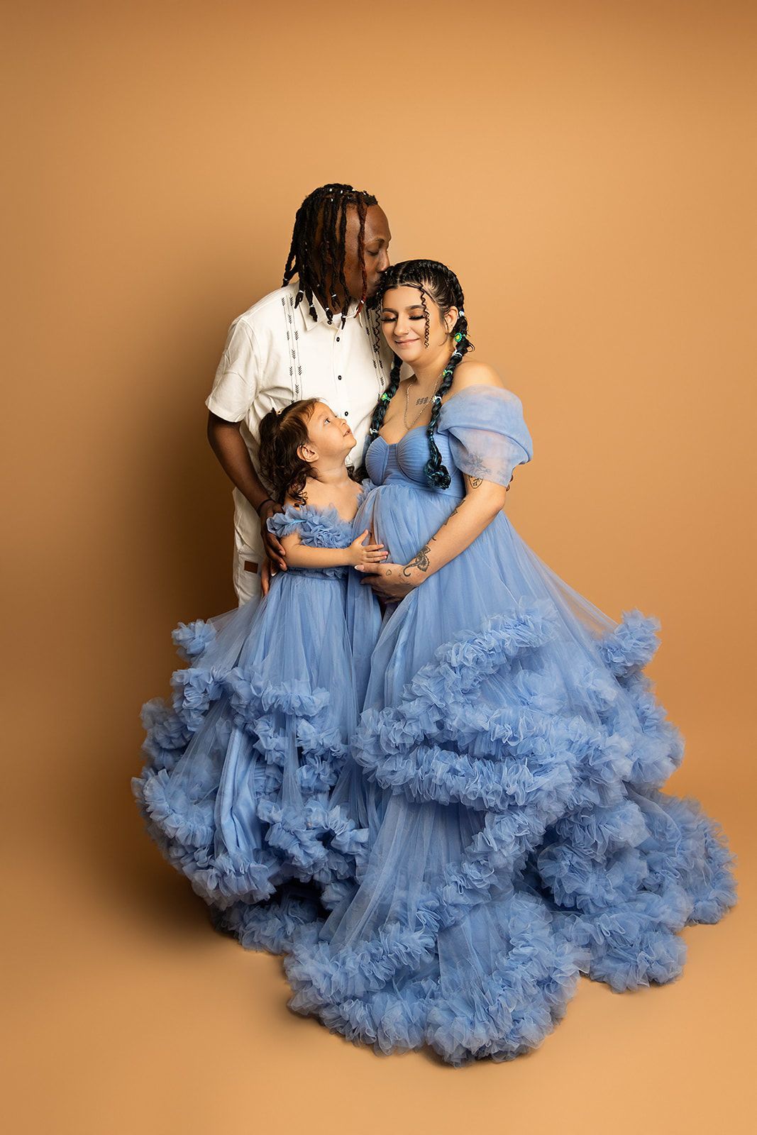 A pregnant woman in a blue dress is posing for a picture with her husband and daughter.