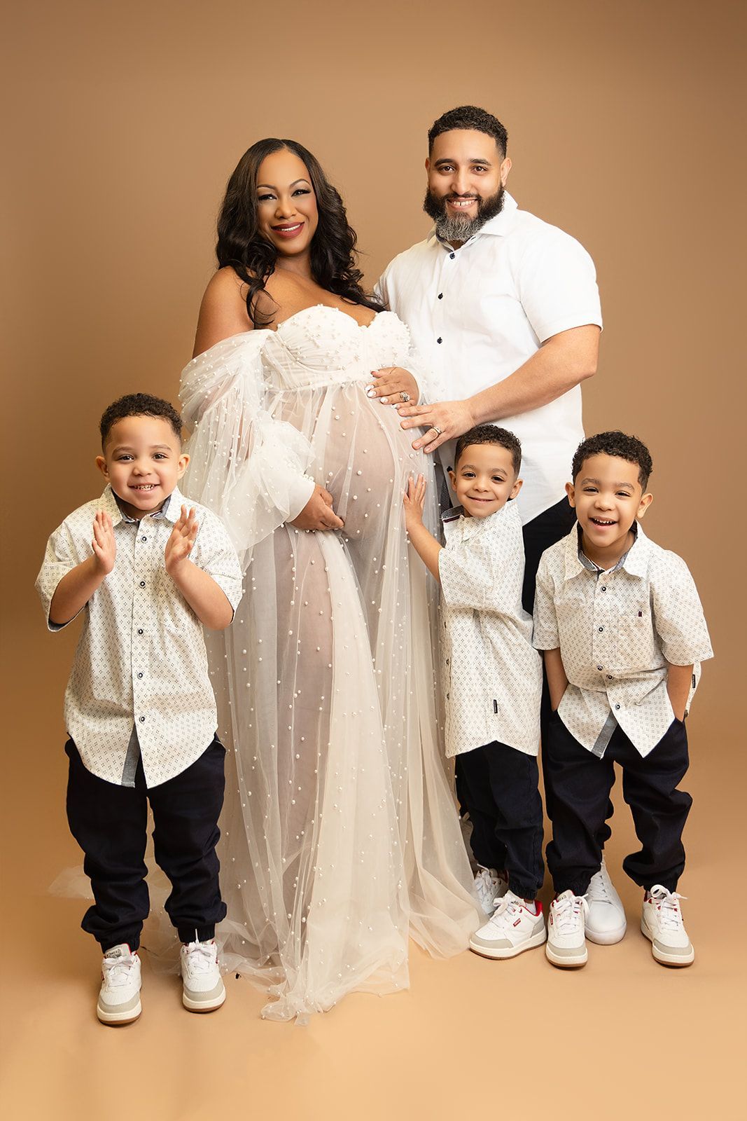 A pregnant woman is posing for a picture with her husband and three sons.