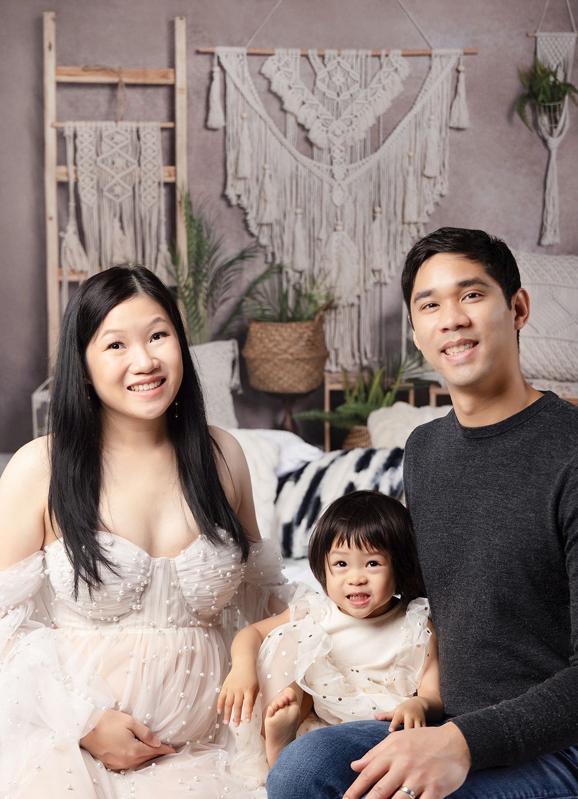 A pregnant woman is posing for a picture with her husband and daughter.