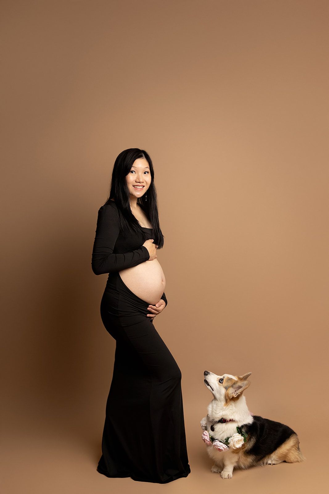 A pregnant woman in a black dress is standing next to a dog.