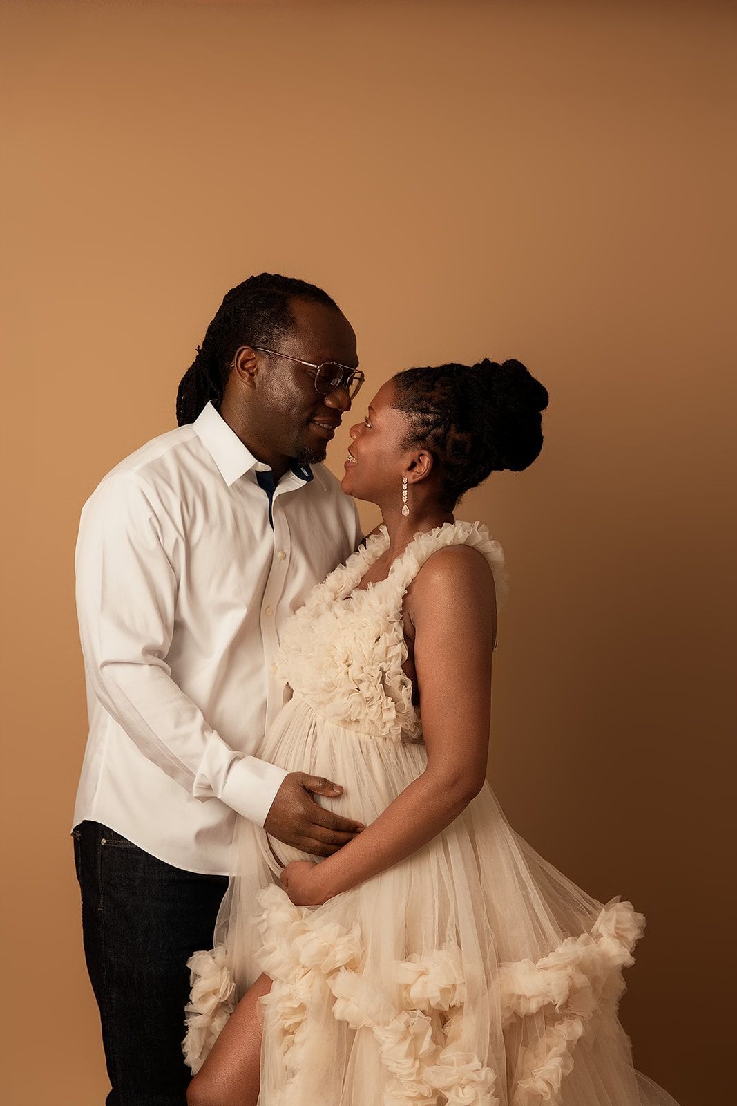 A pregnant woman in a white dress is standing next to a man