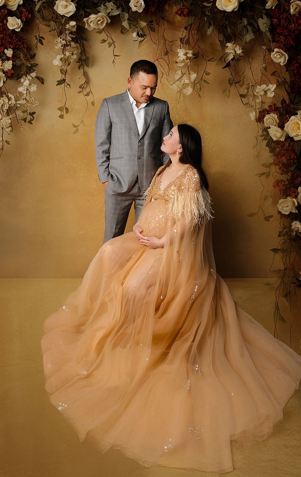 A pregnant woman in a long dress is sitting next to a man in a suit.