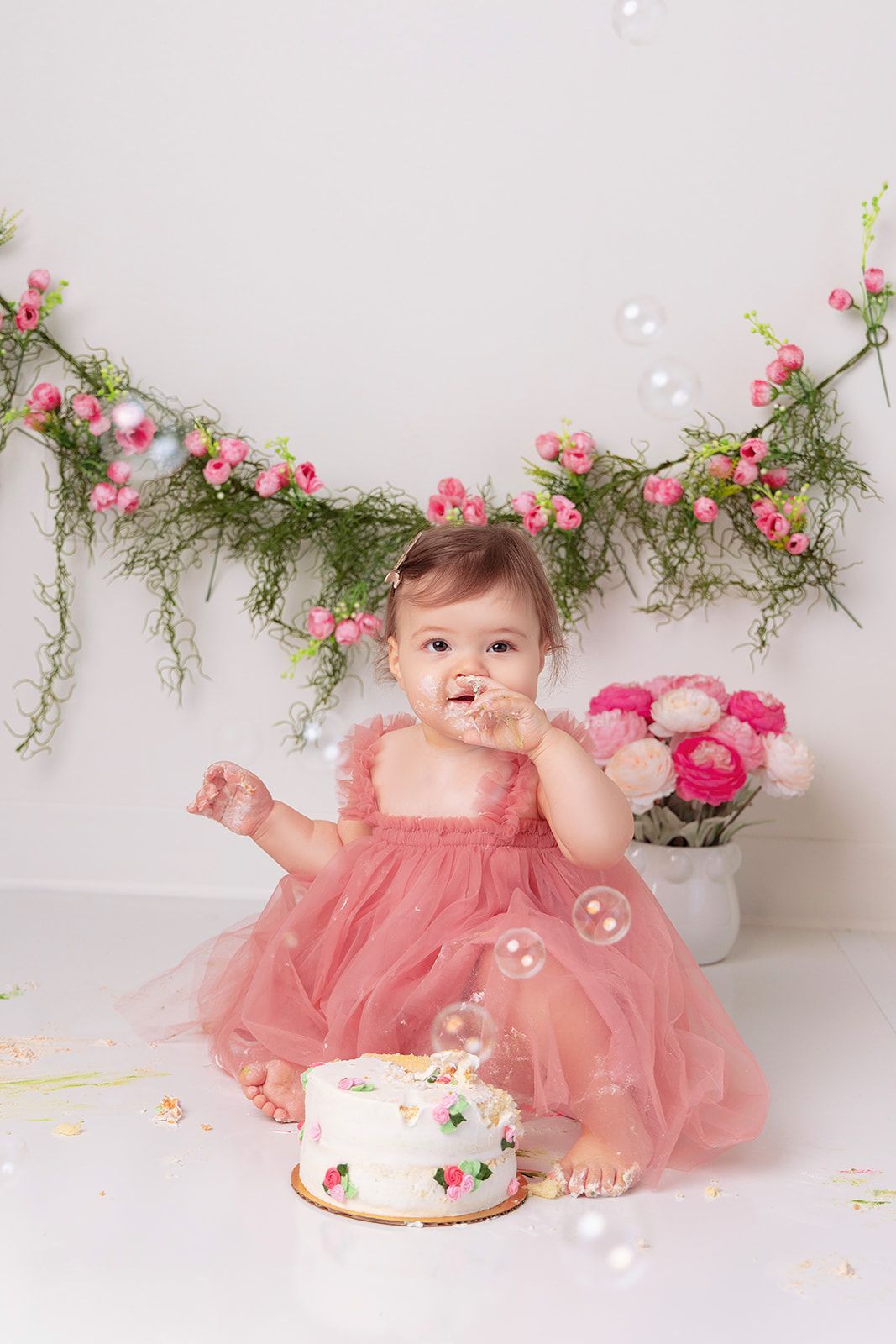 A baby in a pink dress is eating a cake.