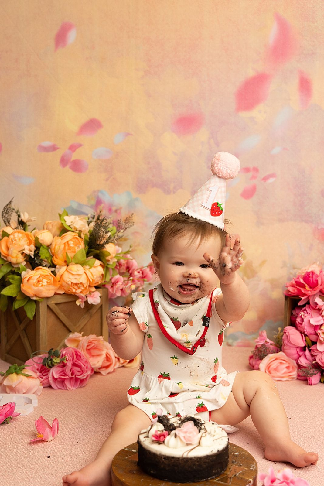 A baby is sitting on a cake with flowers in the background.