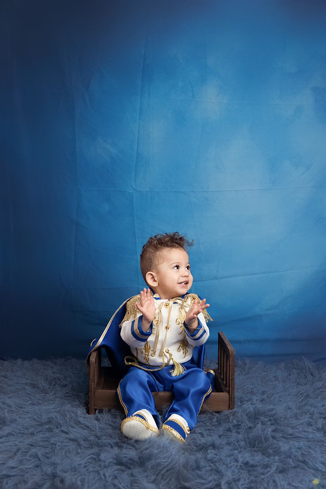 A baby dressed as a prince is sitting in a chair.