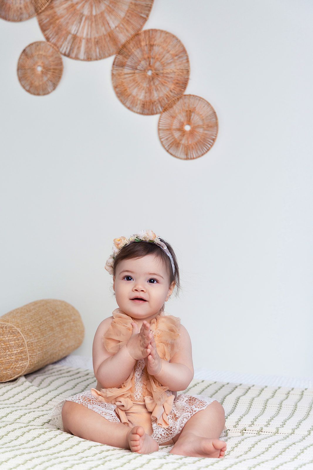 A baby girl is sitting on a bed with her hands together.