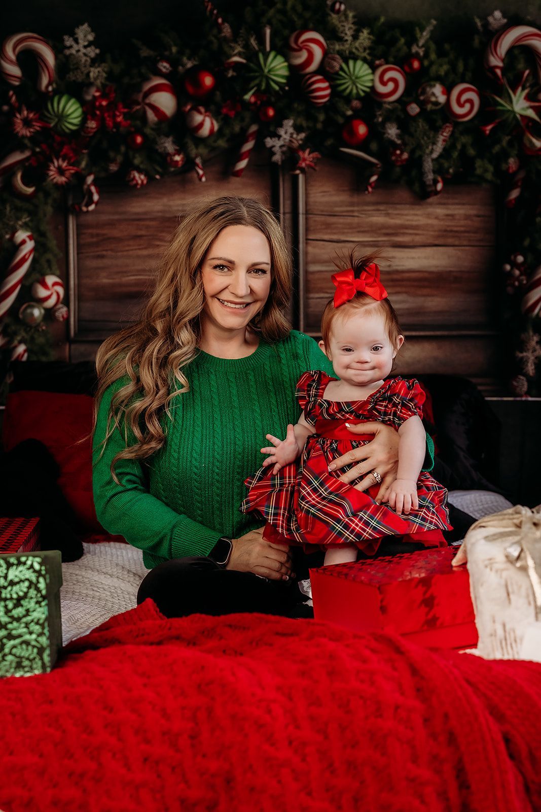 A woman in a green sweater is holding a baby girl in a red dress
