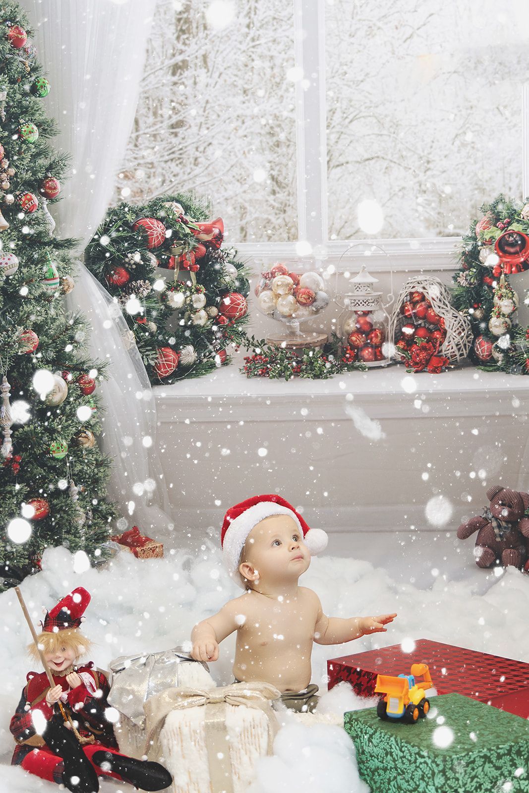 A baby wearing a Santa hat is sitting in front of a Christmas tree